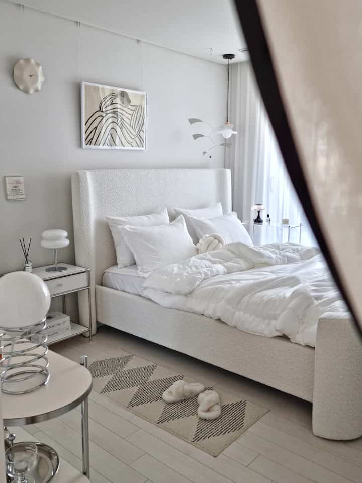 Soft white-tone bedroom featuring a curved fabric bed and simple lighting, creating a modern and clean atmosphere