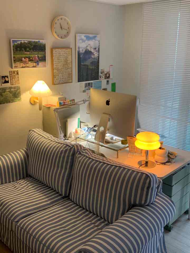 ナチュラルカラーとホワイトが調和したワークスペース、ストライプのソファとiMac、暖かな照明が印象的な居心地の良い書斎空間