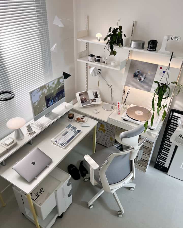 Modern home office in white and gray tones featuring computer desk, ergonomic chair, turntable, and plants in a tidy space