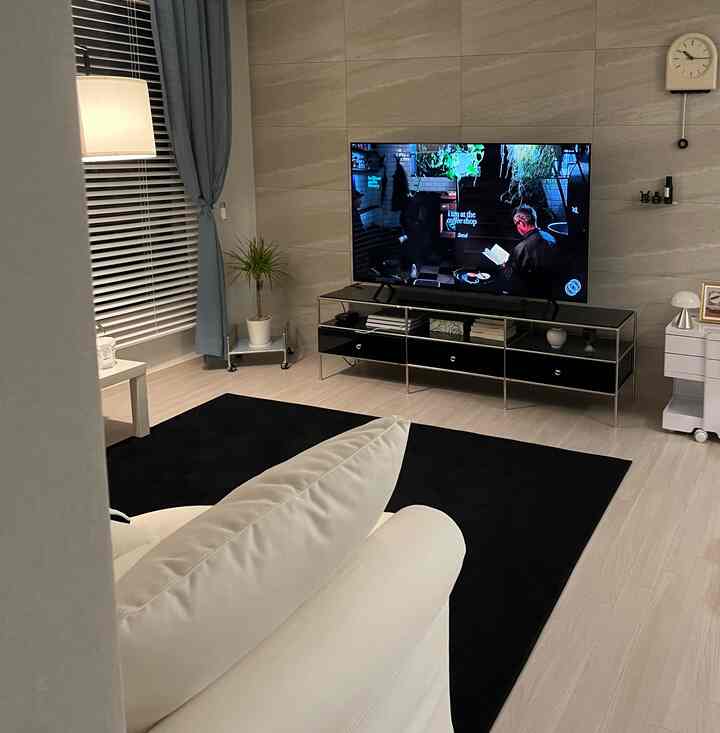 A modern living room in black and ivory tones featuring a rug, sofa, TV stand, and wall clock with a clean aesthetic