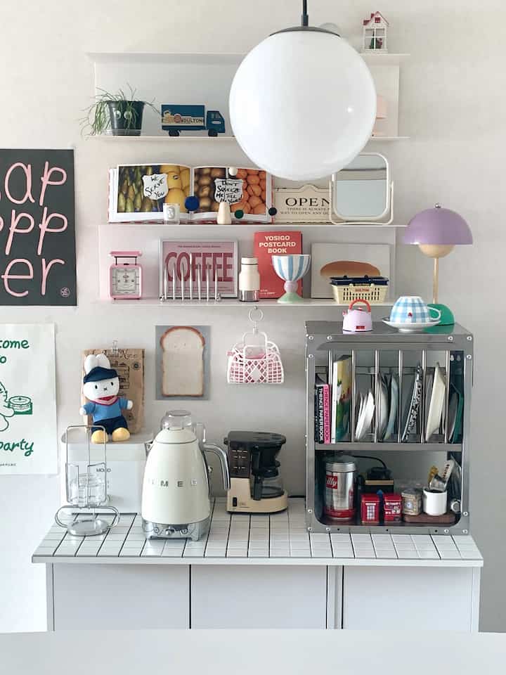 白を基調としたキッチンスペース、タイルカウンターにスメールグの電気ケトルやコーヒーメーカーが置かれ、多様な小物が整頓されたモダンなホームカフェのインテリア