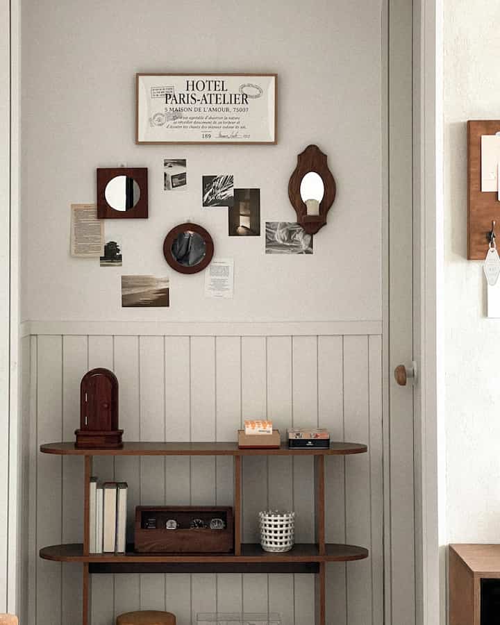 ナチュラルな木目調の廊下、ヴィンテージポストカードと木製の鏡を配した壁装飾と無垢材の棚が配置された印象的な空間
