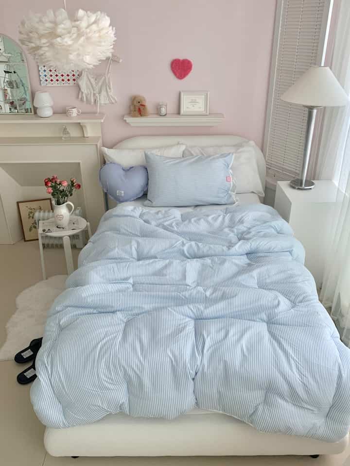 Cozy small bedroom with pale pink walls and sky-blue striped bedding