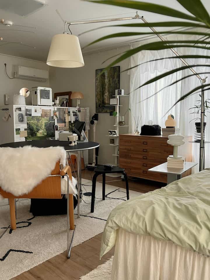 A natural-toned studio apartment in white and brown featuring a bed, desk, and wooden furniture with a cozy atmosphere