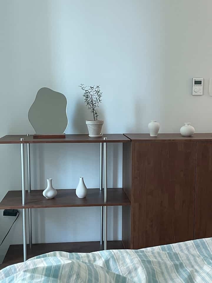 白い壁と濃いブラウンの木製家具が配置された寝室、ミニマルでナチュラルな雰囲気のインテリア