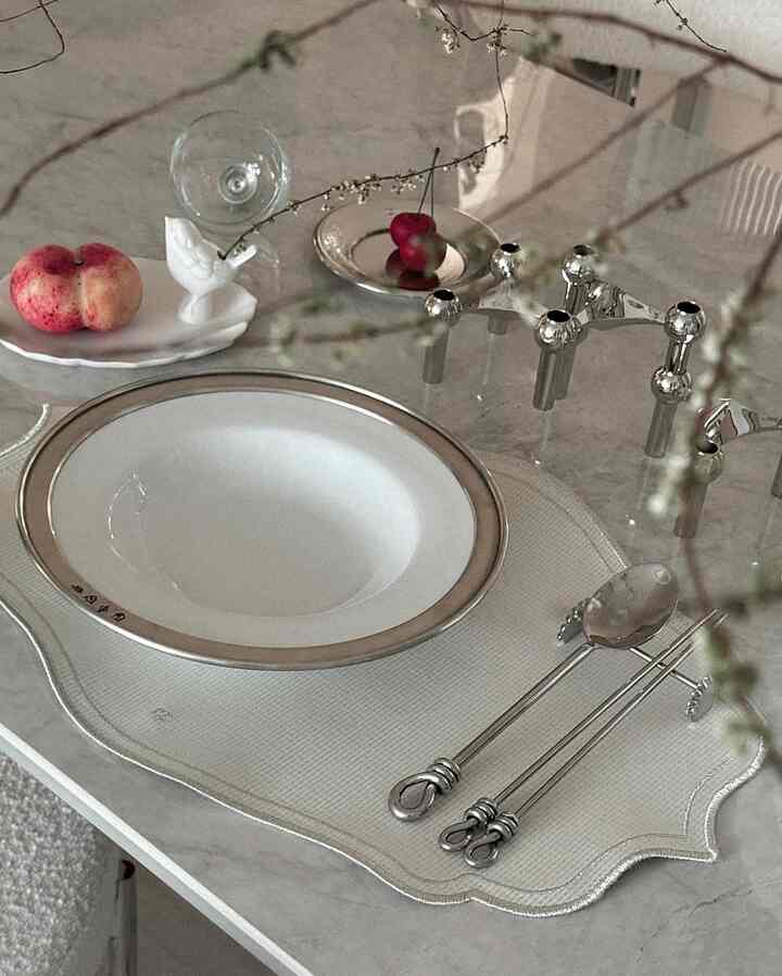White and silver toned dining table featuring cutlery, plate, and candle holder in an elegant setting