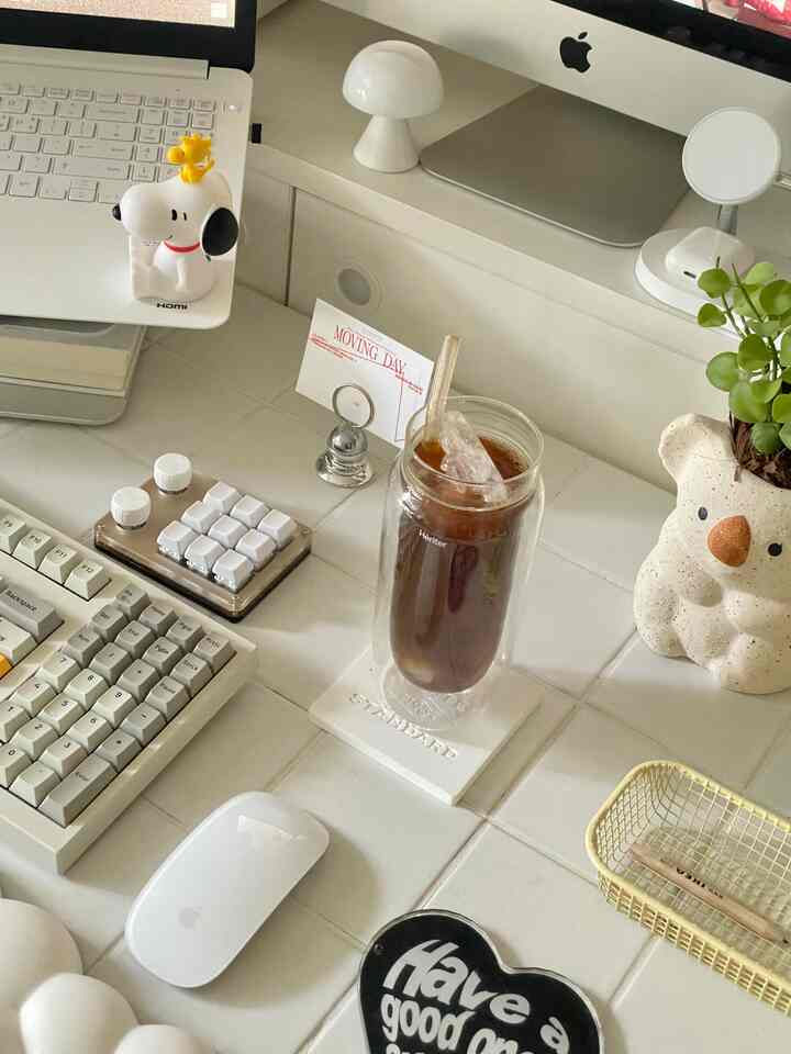 White and silver toned home office space featuring iMac and glass of iced coffee on desk with a clean, cozy work environment