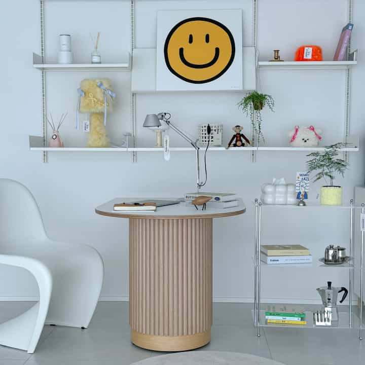 White-walled modern minimal home office featuring a wood-tone round table, white chair, shelves with small objets decor