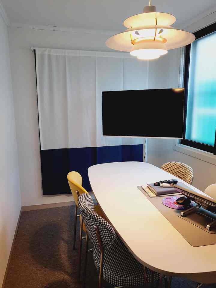 白とネイビーのカーテンがある狭くてモダンなホームオフィス、中央に大きなテーブルと複数のオフィスチェアが配置された印象的な空間