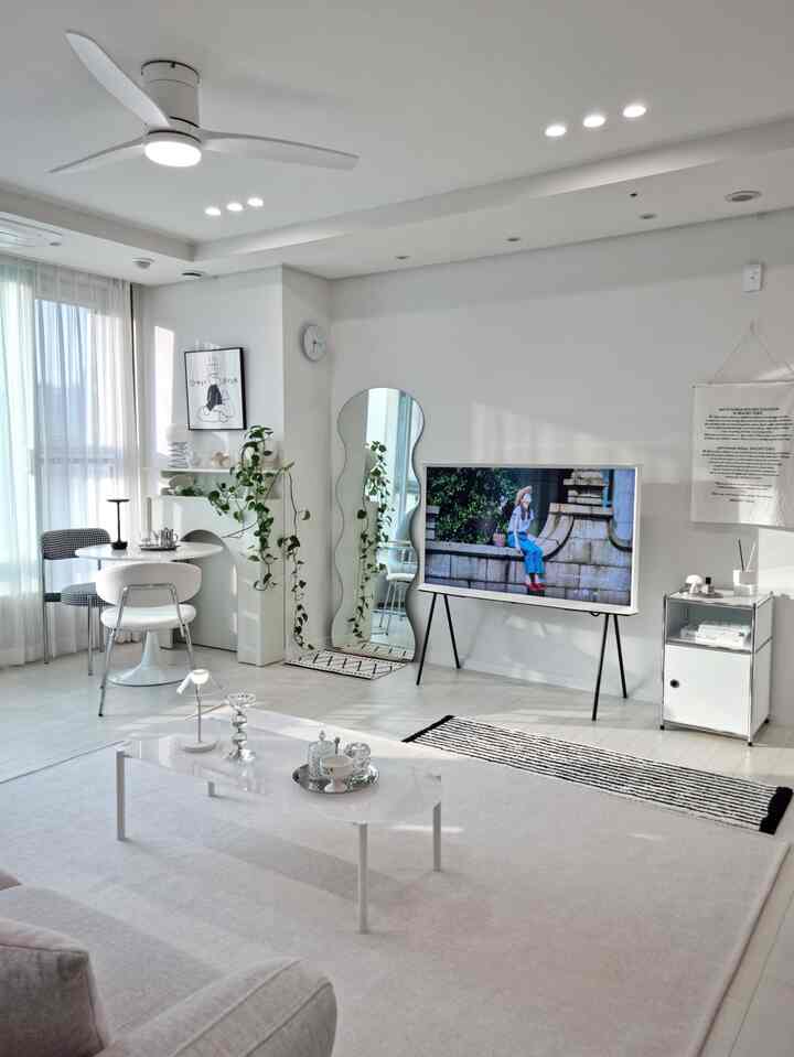 白を基調としたモダンなリビング、ナイトテーブルと全身鏡、テレビスタンドが配置された清潔感のある明るいインテリア