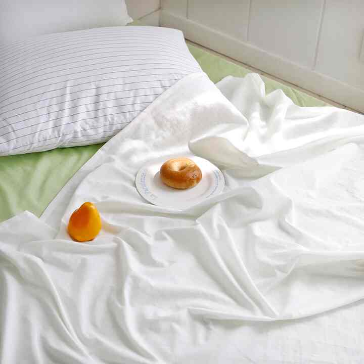 ホワイトとライトグリーンの色調の寝室、枕と寝具が整った落ち着いた雰囲気のあるインテリア