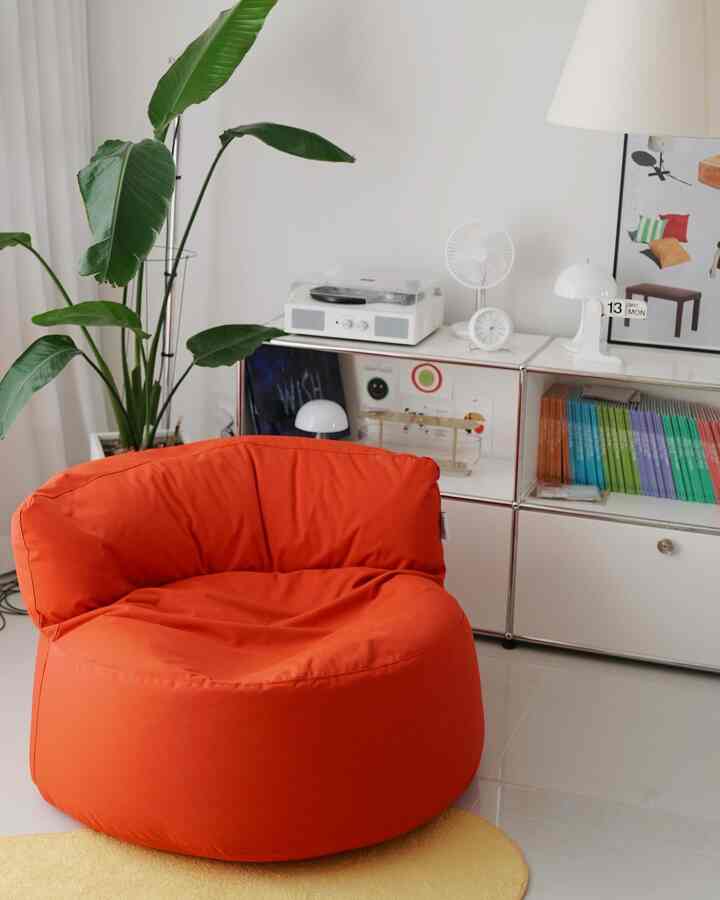 明るいホワイト調のリビング、中央にオレンジのビーズクッションと黄色のラグが配置された温かみのあるインテリア