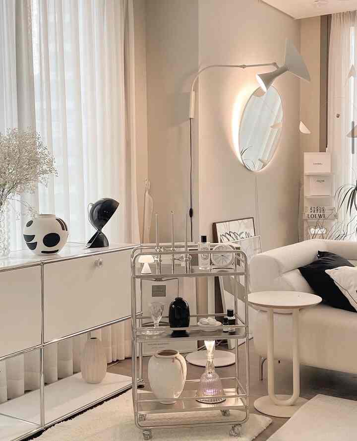 White toned living room featuring a chrome trolley, simple sofa, and lamps creating a modern atmosphere
