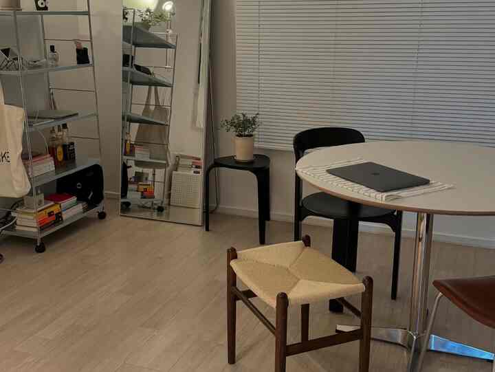 白色とナチュラルカラーが調和したリビング、丸いダイニングテーブルと椅子、棚、スツールが配置された印象的な空間