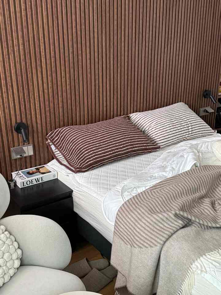 Wood tone wall with soft bedding and nightstand in a cozy bedroom space