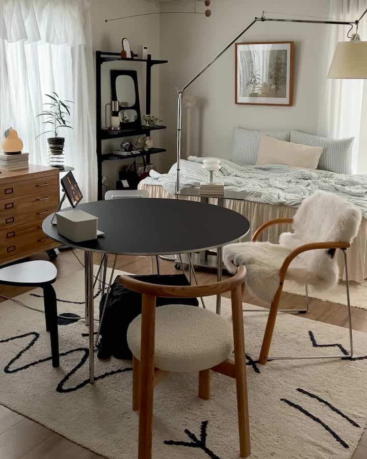 ウッドトーンとブラックが調和する8坪ワンルーム、ベッドとダイニングテーブル、スツールが配置されたナチュラルモダンなインテリア