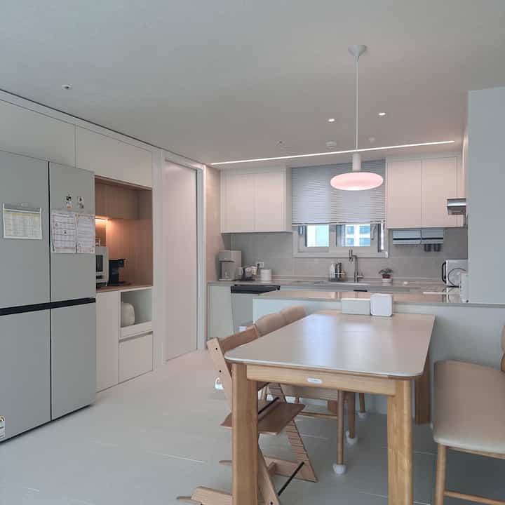 白と木目調のキッチン空間、6人用ダイニングテーブルとペンダントライトが配置されたシンプルで清潔感のあるインテリア