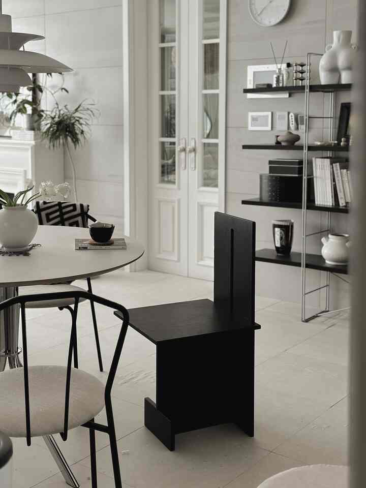 ホワイトとブラックのトーンのダイニングルーム、円形のダイニングテーブルとミッドセンチュリーモダンの椅子が配置された清潔感のある空間