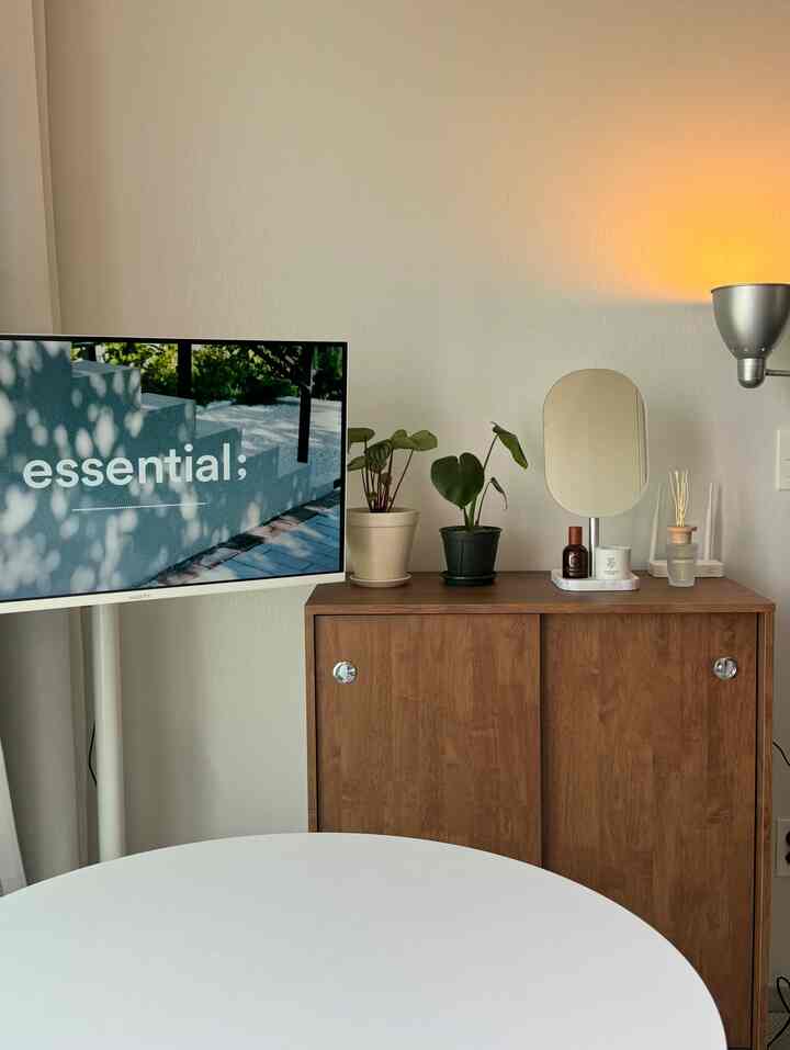 白い壁と木目調キャビネット、小さな植物とテレビ台が配置された清潔感のあるナチュラルなリビング