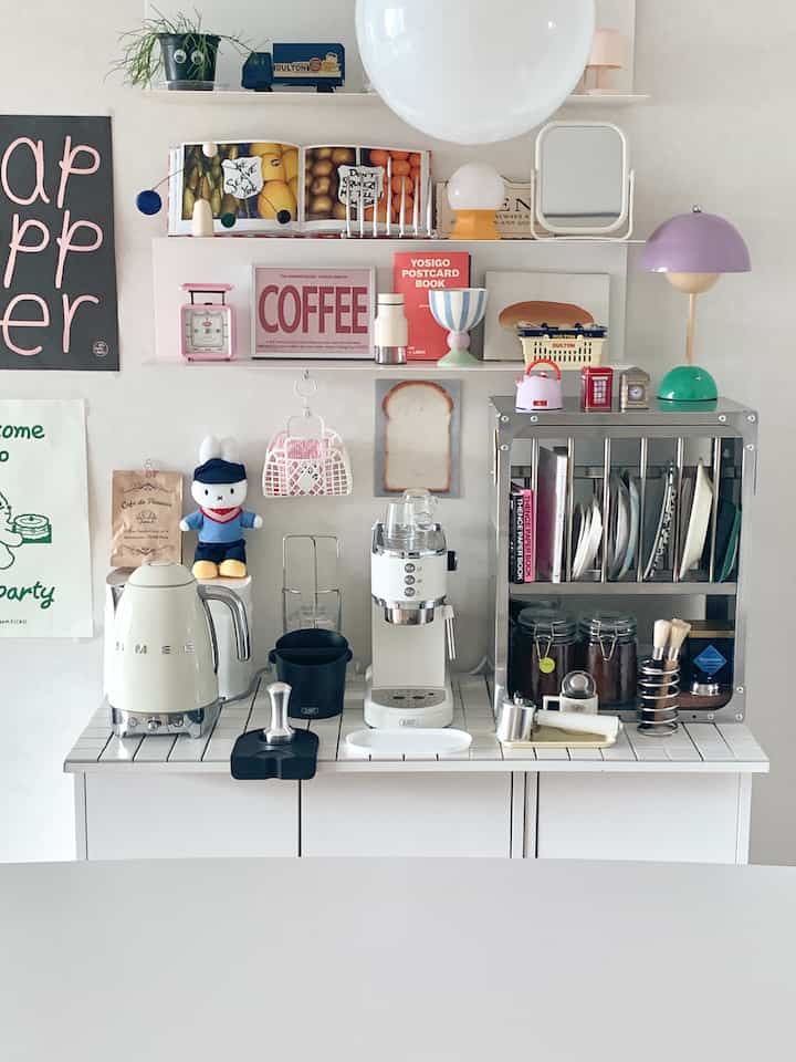 White and natural toned kitchen featuring a sleek espresso machine and shelves displaying coffee accessories in a cozy home cafe space