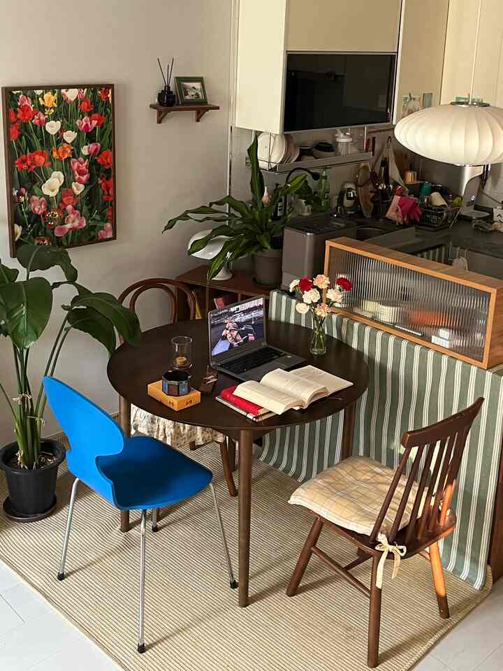 Natural modern kitchen space featuring brown wooden dining table, blue chair, potted plants, and framed artwork