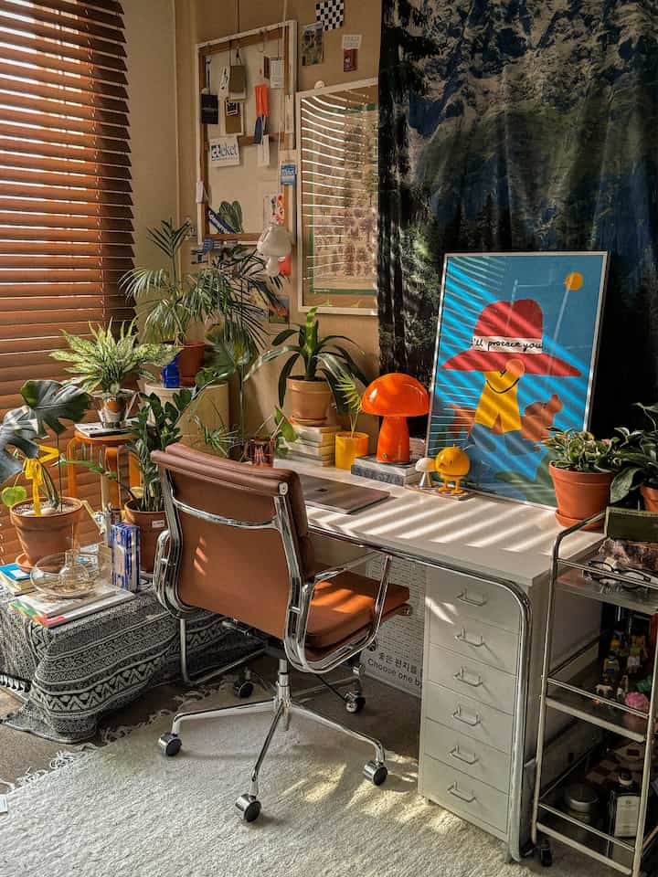 暖かいブラウンとナチュラルなトーンのワンルームホームオフィス、植物とカラフルなポスターが調和した居心地の良い作業空間