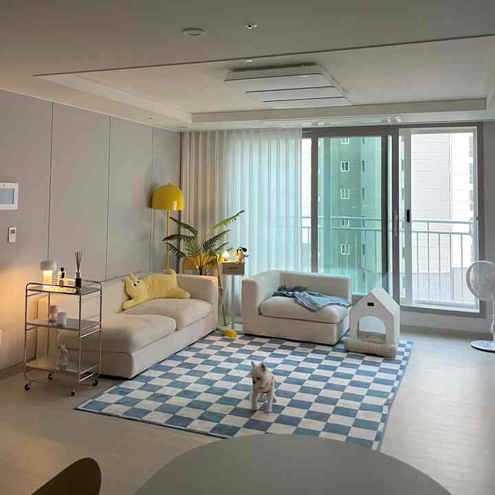 黄色と青のアクセントがあるモダンなリビング、セクショナルソファとチェック柄ラグ、小型ペットの犬とキャットハウスが配置された雰囲気のあるインテリア