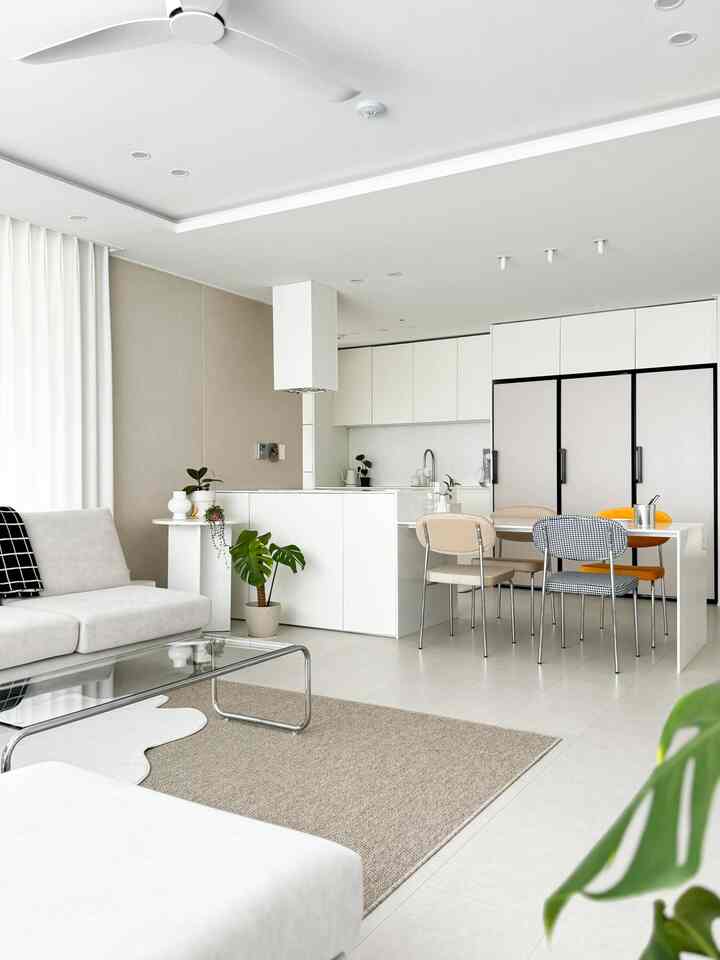 Bright and spacious natural modern living and dining room in white and beige tones featuring sofa, dining table, and open kitchen