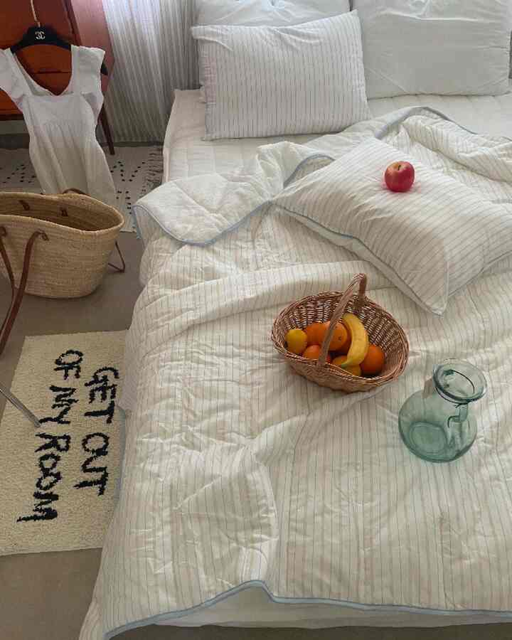 白とナチュラルトーンの寝室、縞模様の寝具とラタンバスケットが配置されたヴィンテージ感のあるインテリア