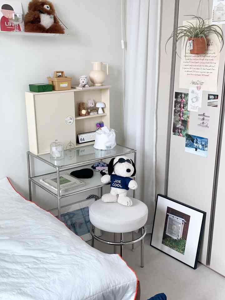 白と木目調が調和した小さな寝室、ガラス棚と化粧台にかわいい小物が置かれた雰囲気のあるインテリア