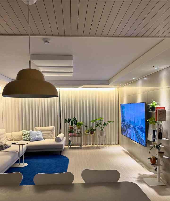 白と木目調が調和するリビング、ベージュのソファと青いラグ、多様な植物が配された雰囲気のあるインテリア