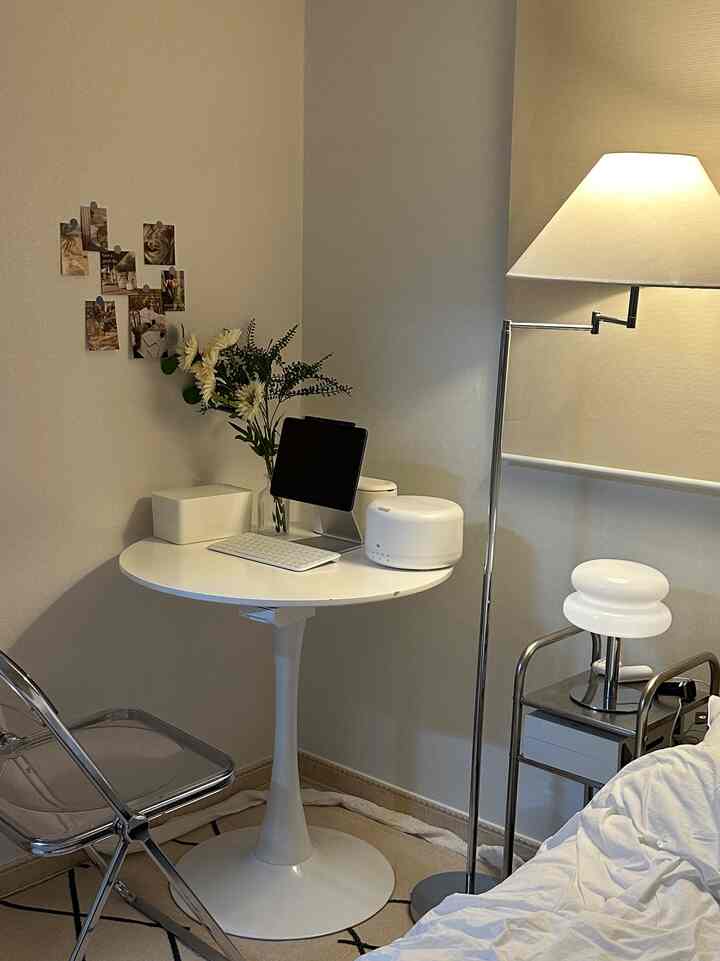 ホワイトとナチュラルトーンのコンパクトな寝室、丸テーブルとフロアランプが配置されたミニマルなホームオフィス空間