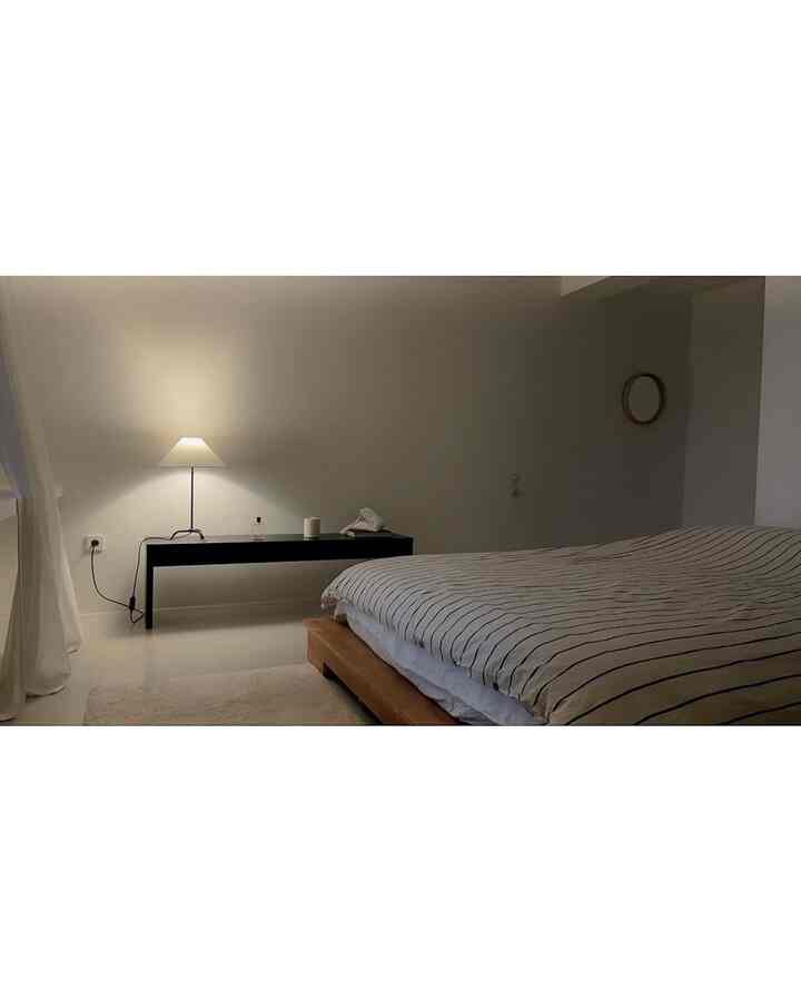 白と黒、木目調が調和したミニマルな寝室、木製ベッドフレームとフロアランプが落ち着いた雰囲気を醸し出す空間