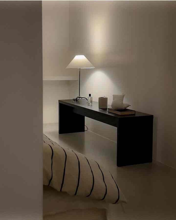 ベージュと黒のトーンの寝室、ストライプのベッドカバーと黒いベンチ、テーブルランプが調和するミニマルなインテリア