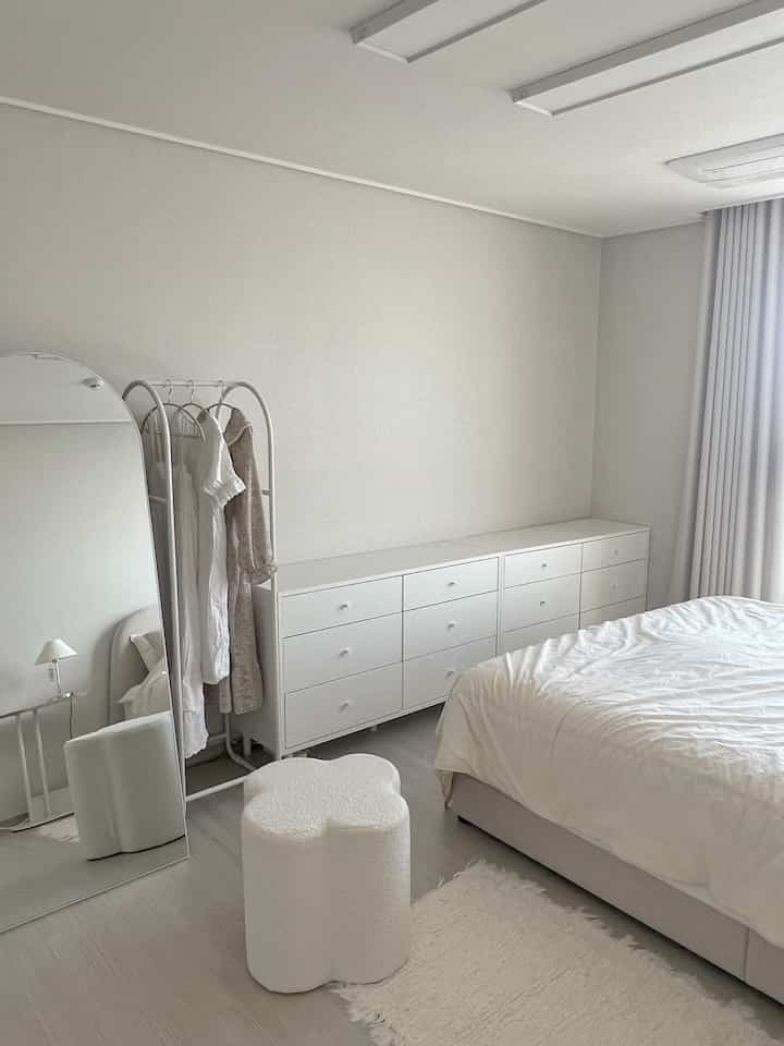 White and beige toned bedroom featuring a dresser, arch coat rack, and boucle stool with a natural atmosphere