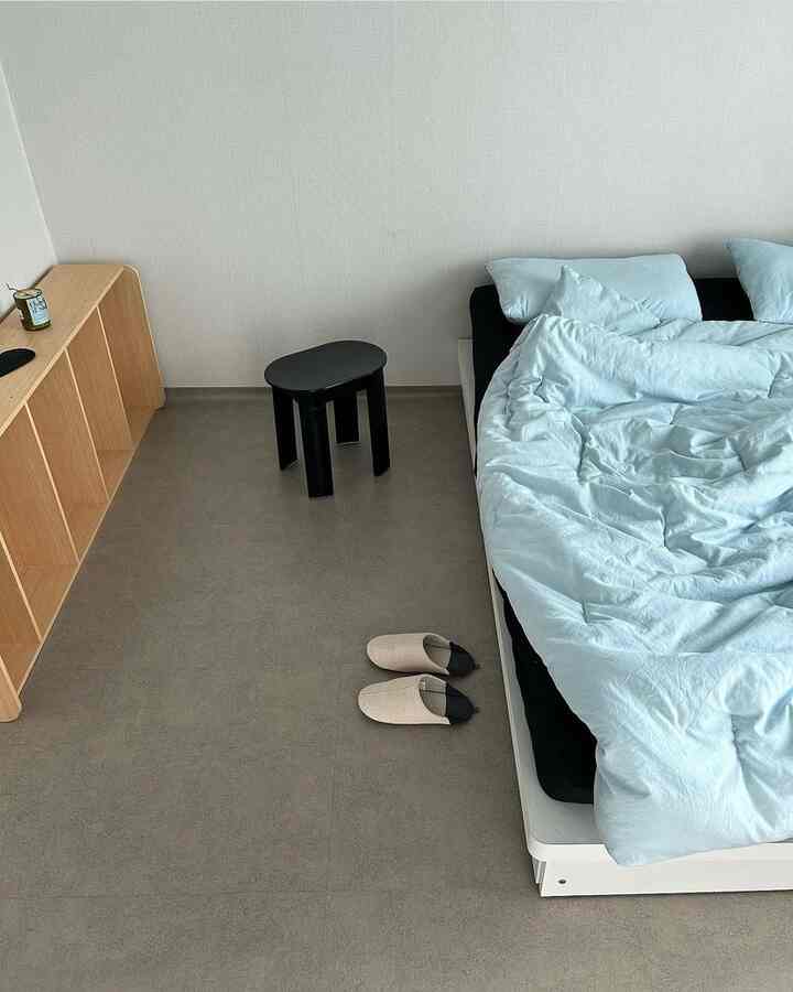 明るいトーンのミニマルな寝室、黒のマットレスカバーとパステルブルーの寝具が配置された清潔感のあるインテリア