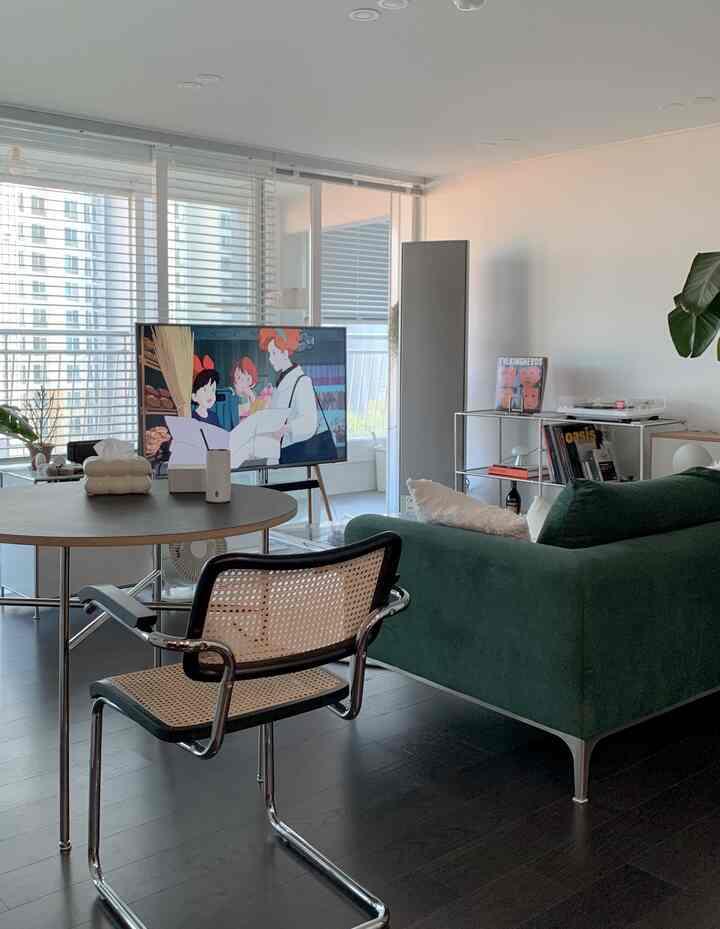 白い壁とダークブラウンの床のリビング、緑のソファとラタンのダイニングチェアが配置されたモダンでミニマルな空間