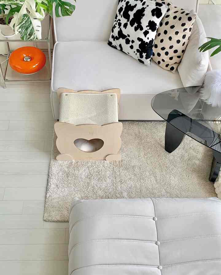 White and beige toned living room featuring a white sofa, modern coffee table, cat house, and plants creating a cozy atmosphere