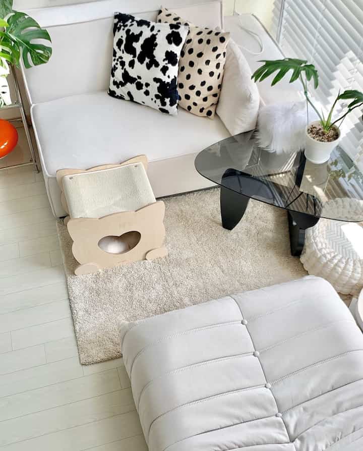 白とベージュの落ち着いた色調のリビング、モジュールソファと猫の隠れ家、ガラスのコーヒーテーブルが配置された印象的な空間