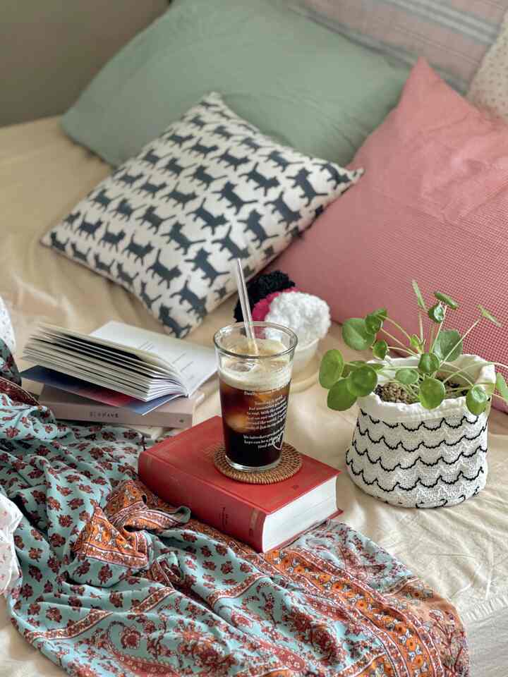 Beige and green toned bedroom featuring patterned fabric, cat-print cushion, and a refreshing plant creating a cozy vintage atmosphere