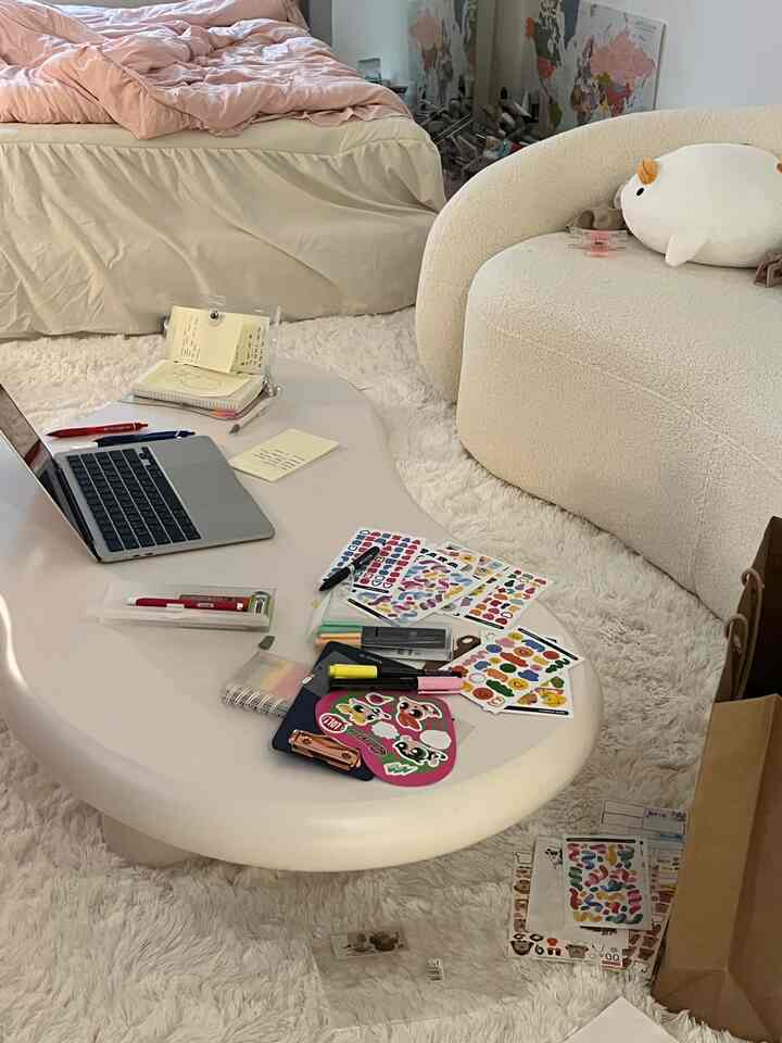 ナチュラルなベージュトーンの寝室兼ホームオフィス、柔らかいソファと曲線的なコーヒーテーブルが配置された雰囲気のあるインテリア