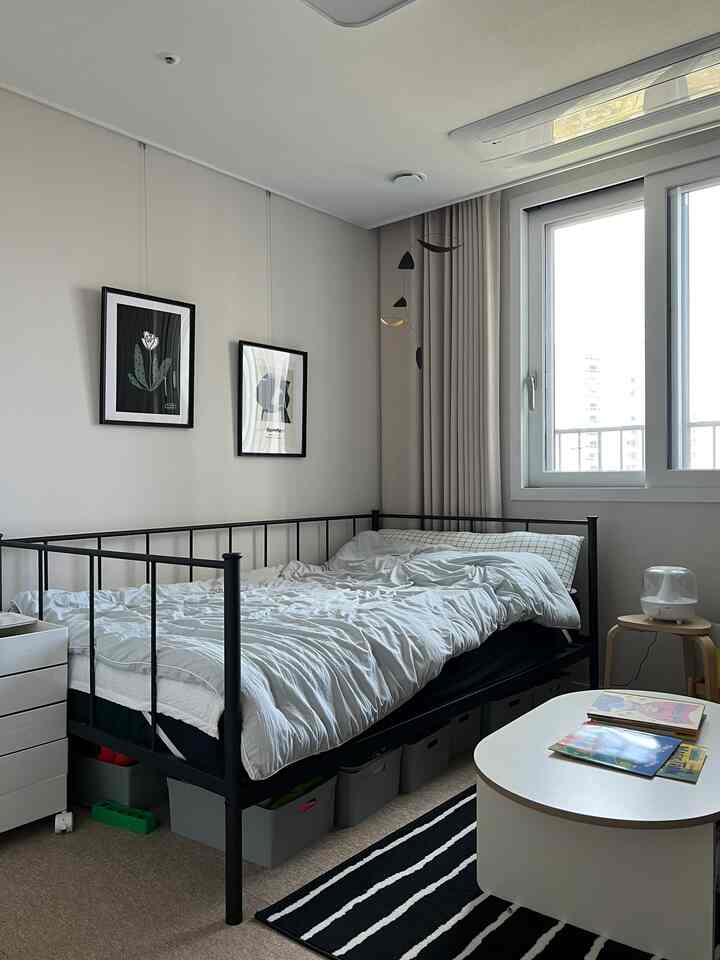 ベージュの色調の子供部屋、黒いメタルベッドと白い寝具、ベッド下に収納ボックスが配置されたシンプルでモダンな空間