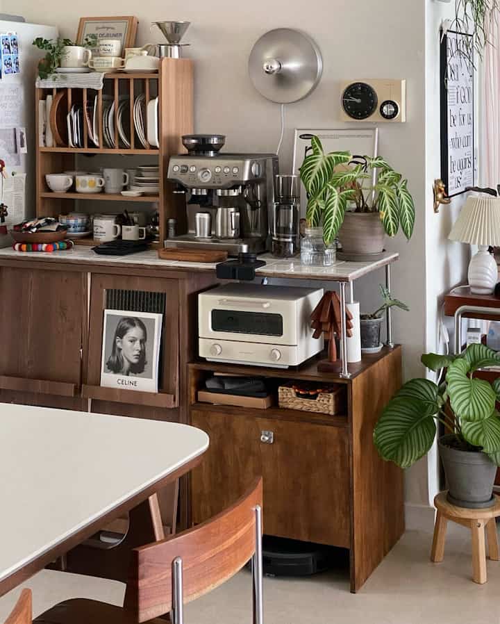 ブラウンの木目調と白いタイル天板が調和した居心地の良いキッチンのおうちカフェ空間、様々な家具と植物が配置されている