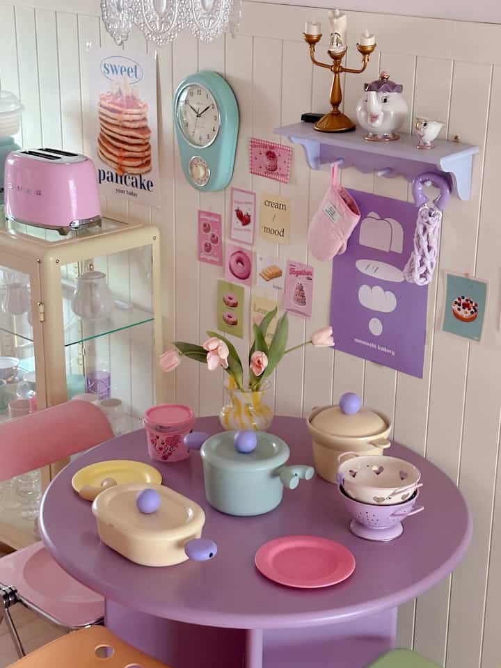 Cute kitchen space in pink and lavender tones featuring a Liberte wall clock and kitchen utensils with charming decor