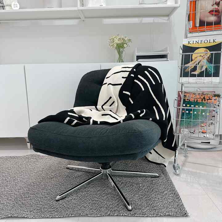 Modern living room with white walls and shelves, black fabric armchair draped with a patterned throw blanket