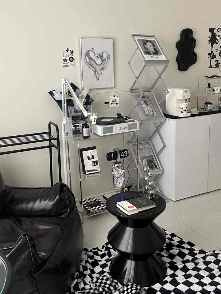 黒とモノトーンのリビングルーム、黒いビーンバッグとスツール、透明な棚とアートポスターが調和した洗練されたインテリア