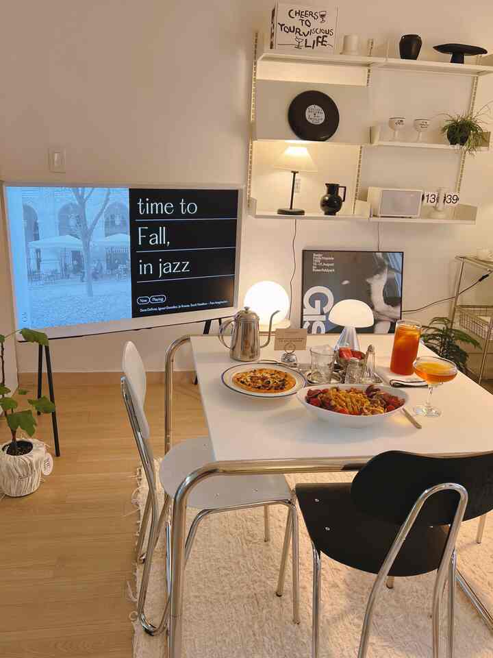 明るいホワイトトーンと木目の床が特徴のリビング、ミッドセンチュリーモダンの家具と照明が配置されたシンプルなホームクック空間