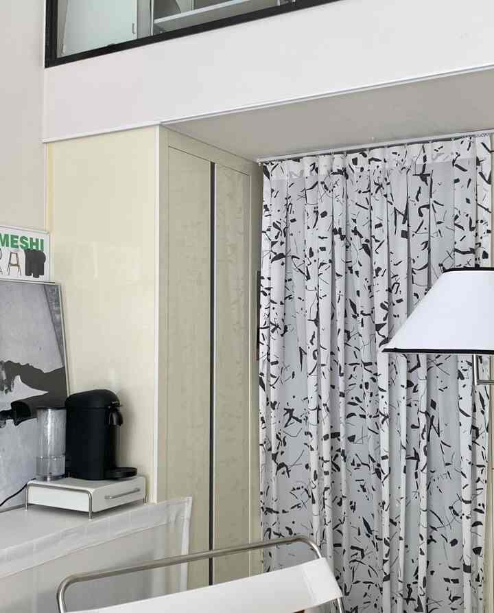 White-toned living space featuring a coffee machine corner, patterned curtains, and floor lamp with a modern cozy atmosphere