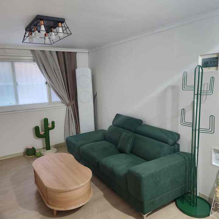 ホワイトの壁と天井が背景のリビング、グリーンのソファと木目調のコーヒーテーブル、サボテン型の爪とぎとコートラックが配置された雰囲気のあるインテリア