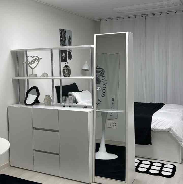 ホワイトの壁とカーテン、ブラックとホワイトの寝具、収納棚、全身鏡が配置されたシンプルなモノトーンの寝室